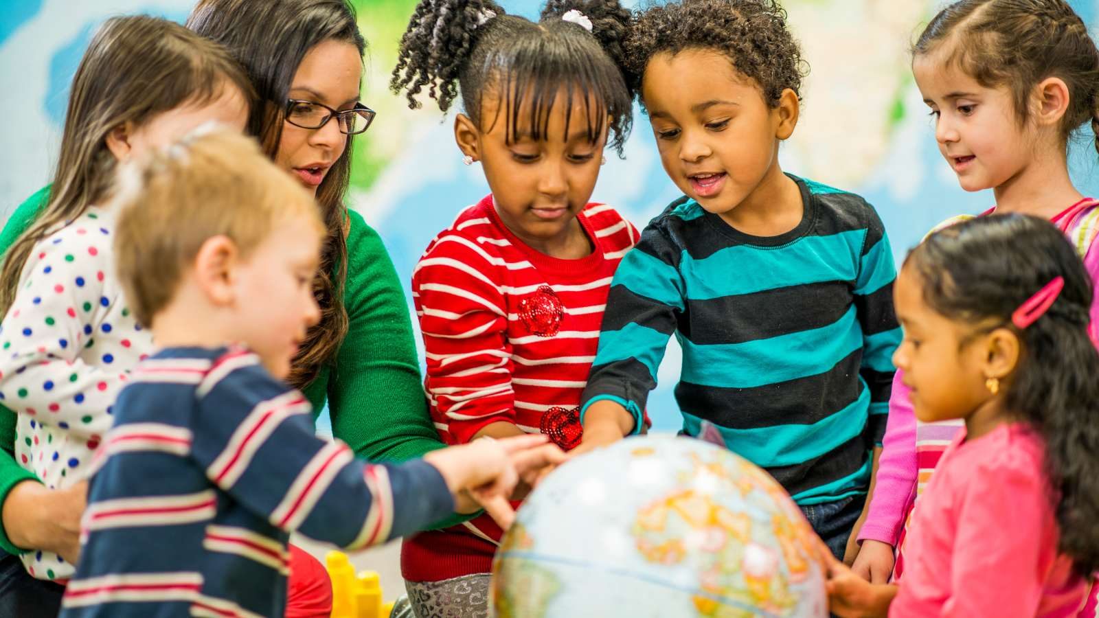 A teacher and young children gathered around a globe